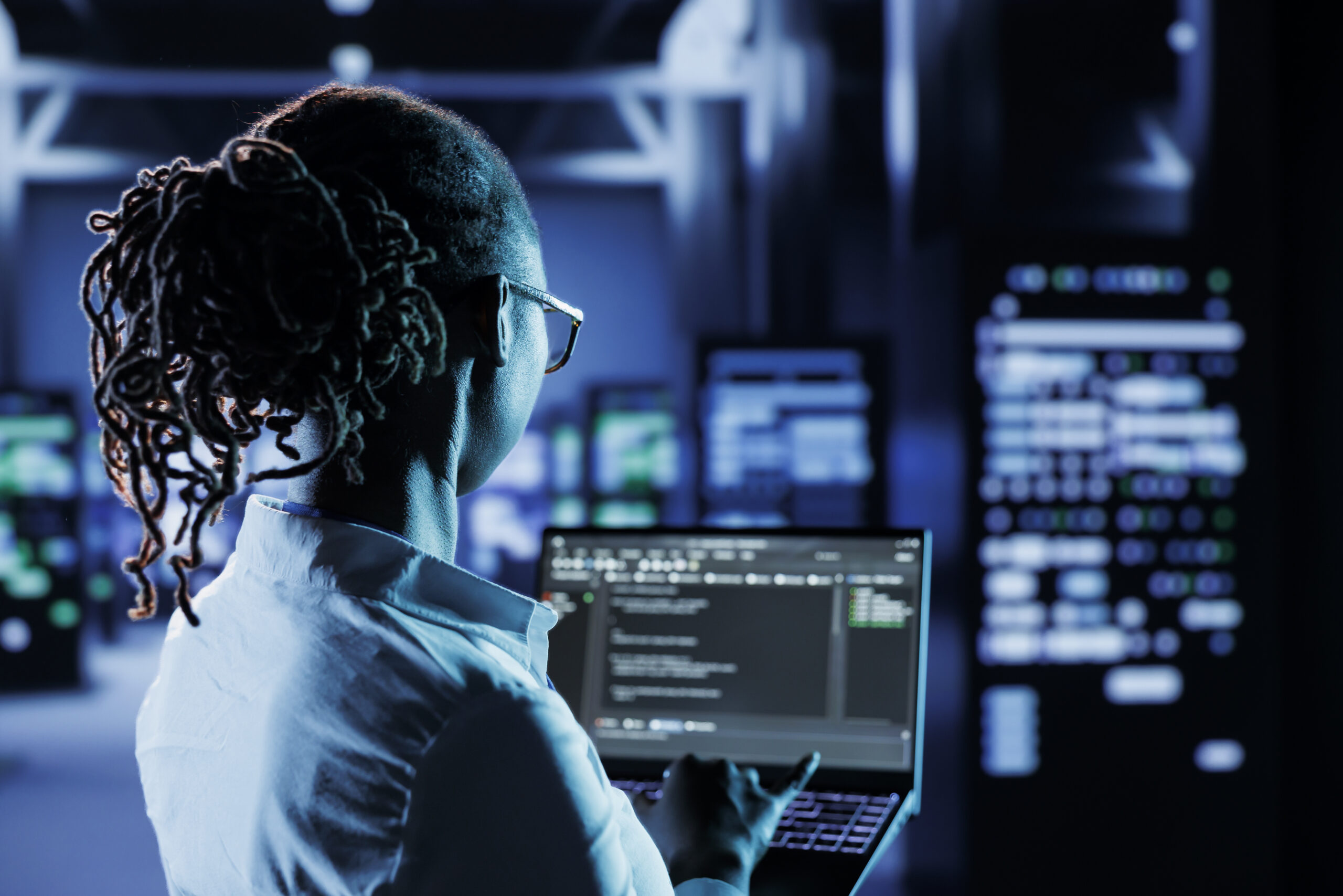 A cybersecurity professional analyzing code on a laptop in a high-tech data center