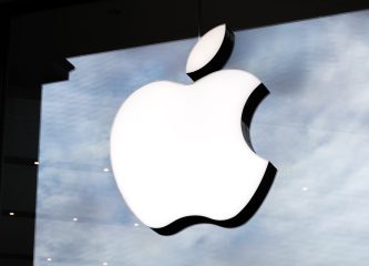 Illuminated Apple logo on a glass storefront with a cloudy sky reflection in the background